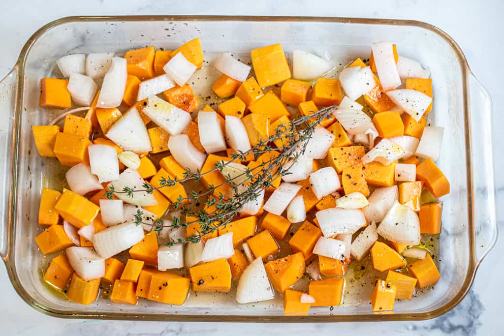 a pan with cut up butternut squash and onion topped with thyme.