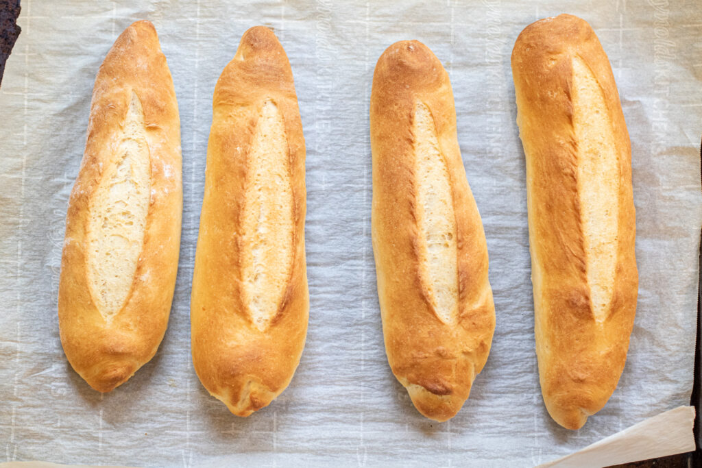 fresh baked baguettes on parchment paper on a baking sheet
