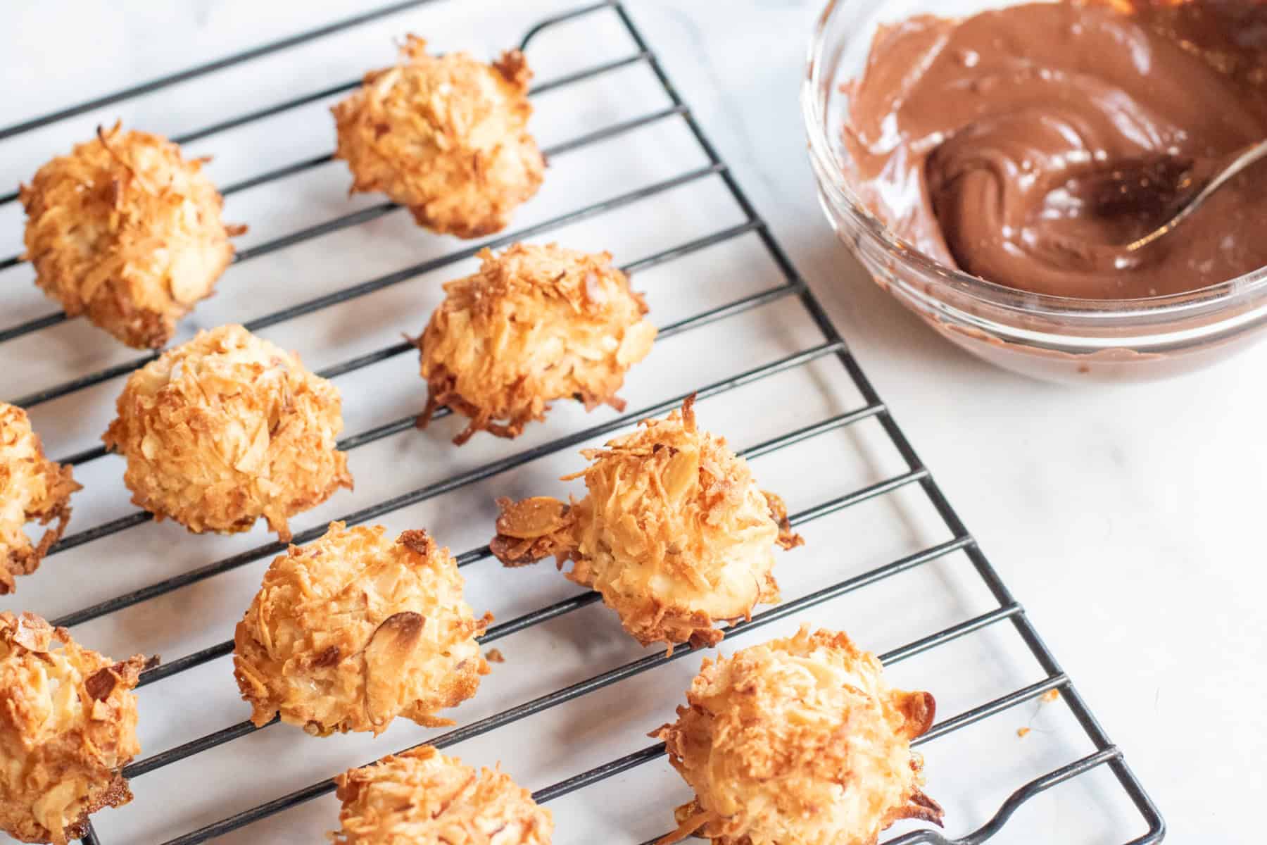cooked maracroons on a cooling tray and a bowl of melted chocolate.