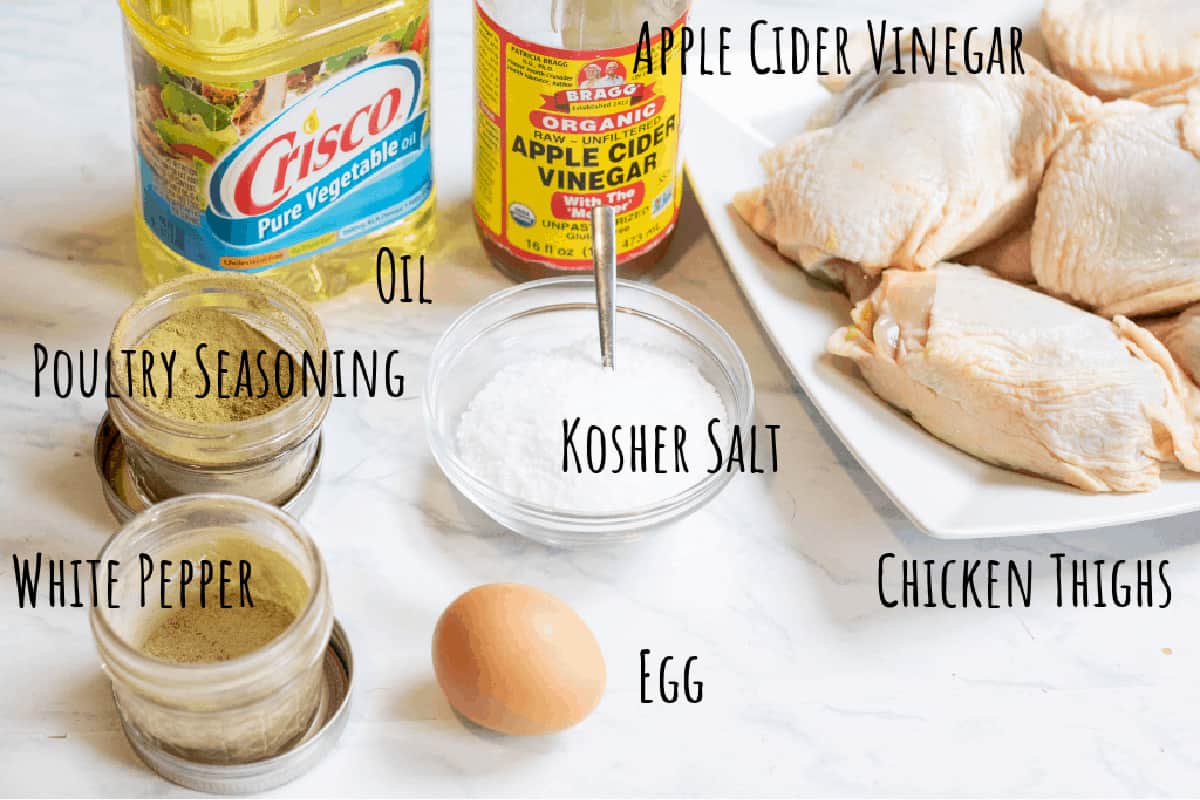 oil, vinegar, raw chicken thighs, egg, salt, poultry seasoning, white pepper on a counter.