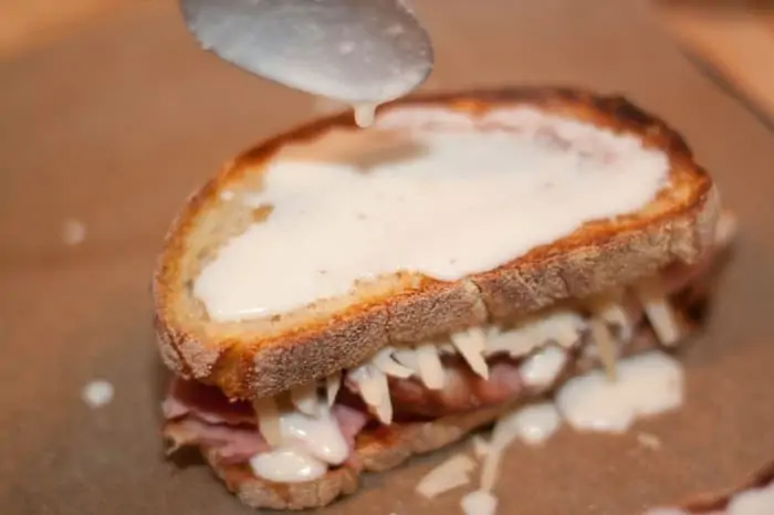 béchamel being spooned on the top of a sandwich.