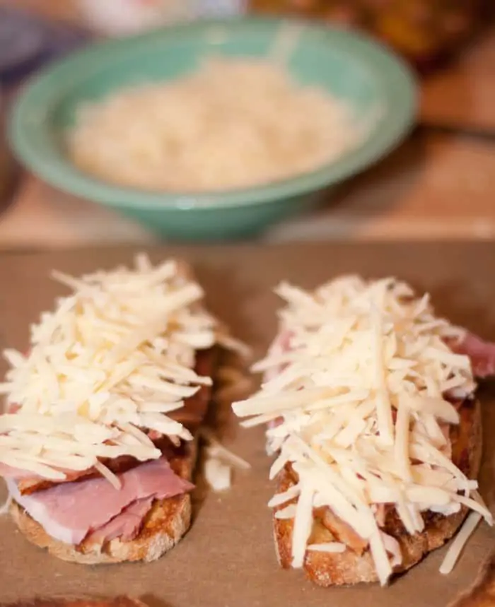 two slices of bread topped with ham and shredded cheese.