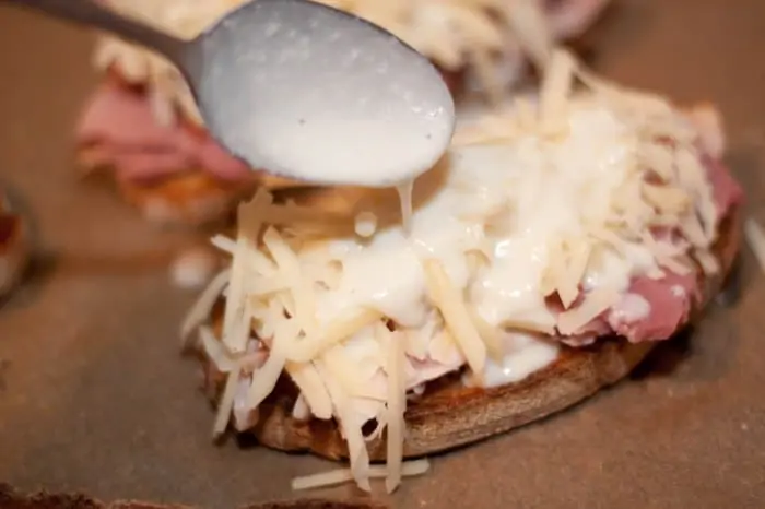 a spoon pouring béchamel sauce on cheese.