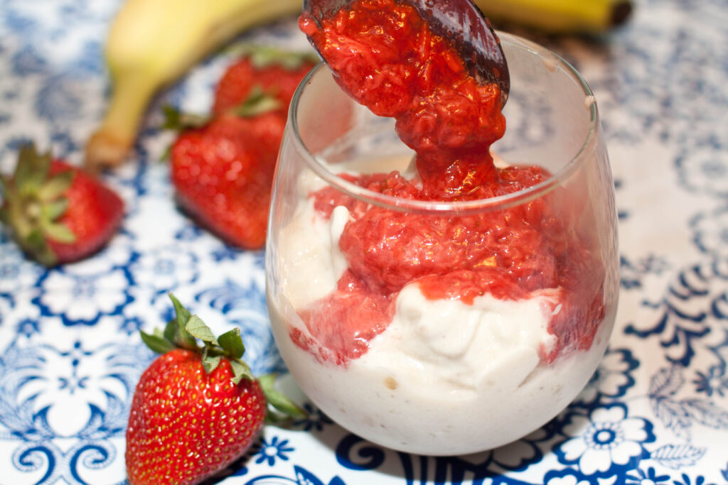 a glass with soft ice cream and a spoon pouring strawberry sauce on top.