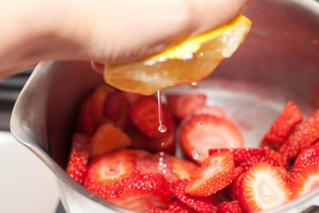 a hand squeezing fresh lemon juice on strawberries.