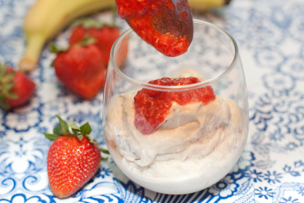 a glass with soft ice cream and a spoon pouring strawberry sauce on top.