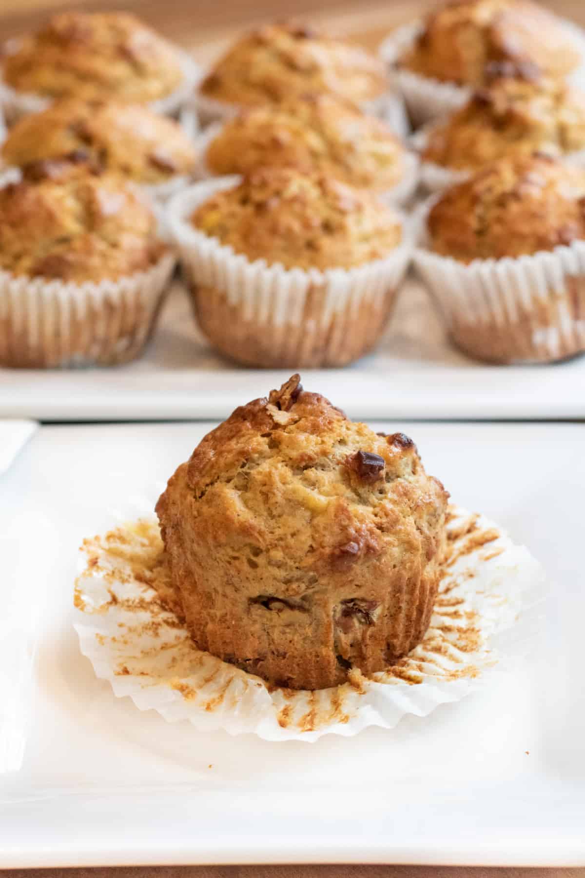 an unwrapped muffin on a plate in front of a plate of muffins.