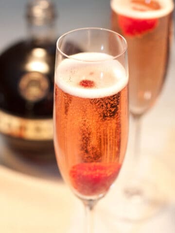 a glass of sparkling pink wine with a raspberry.
