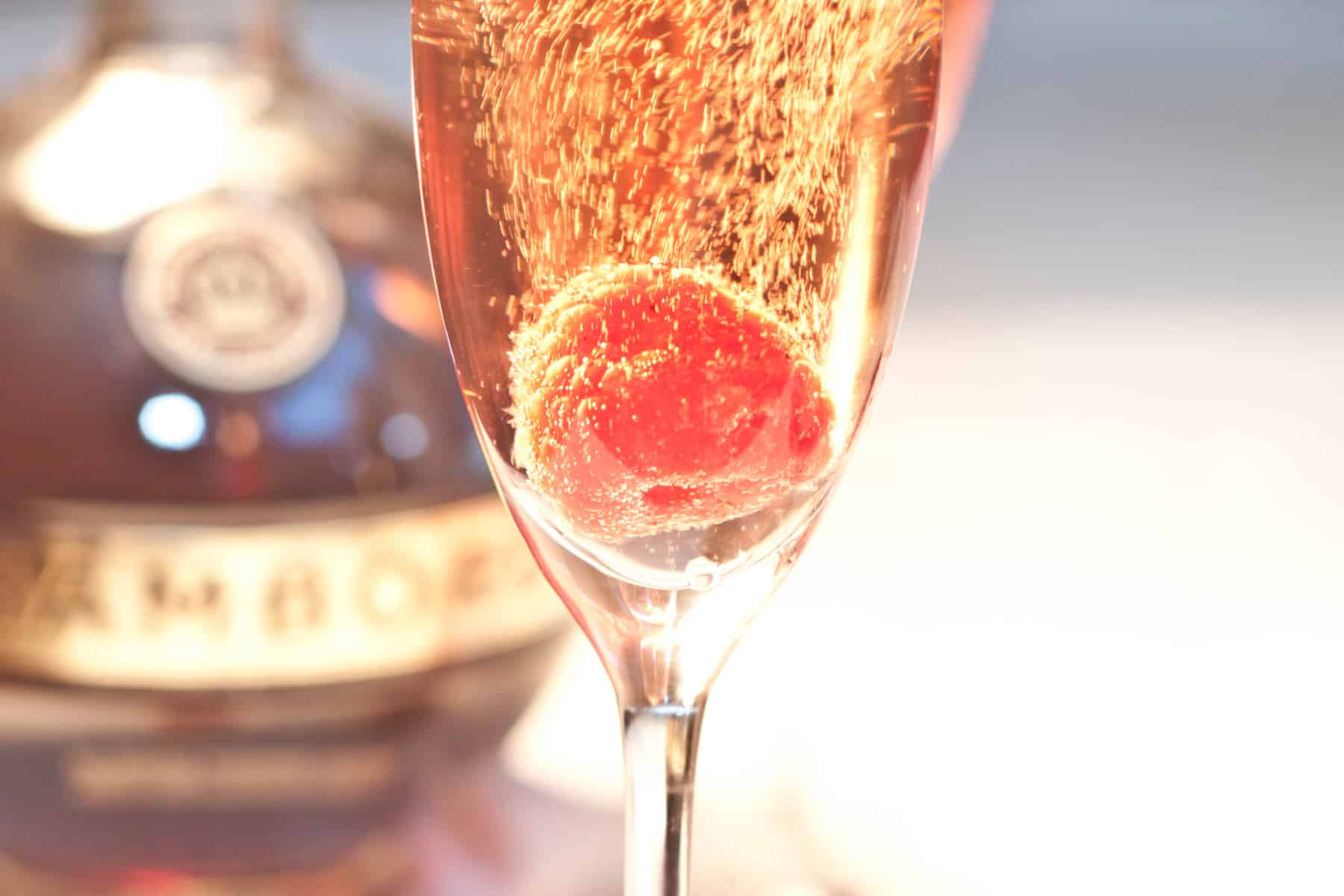 a glass of sparkling pink wine with a raspberry.