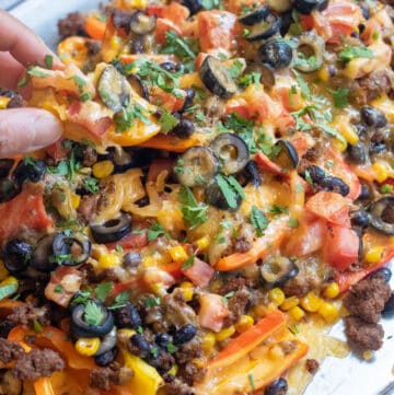 a baking sheet of mini peppers with ground beef, olives, black beans, corn, melted cheese, and fresh cilantro nachos.