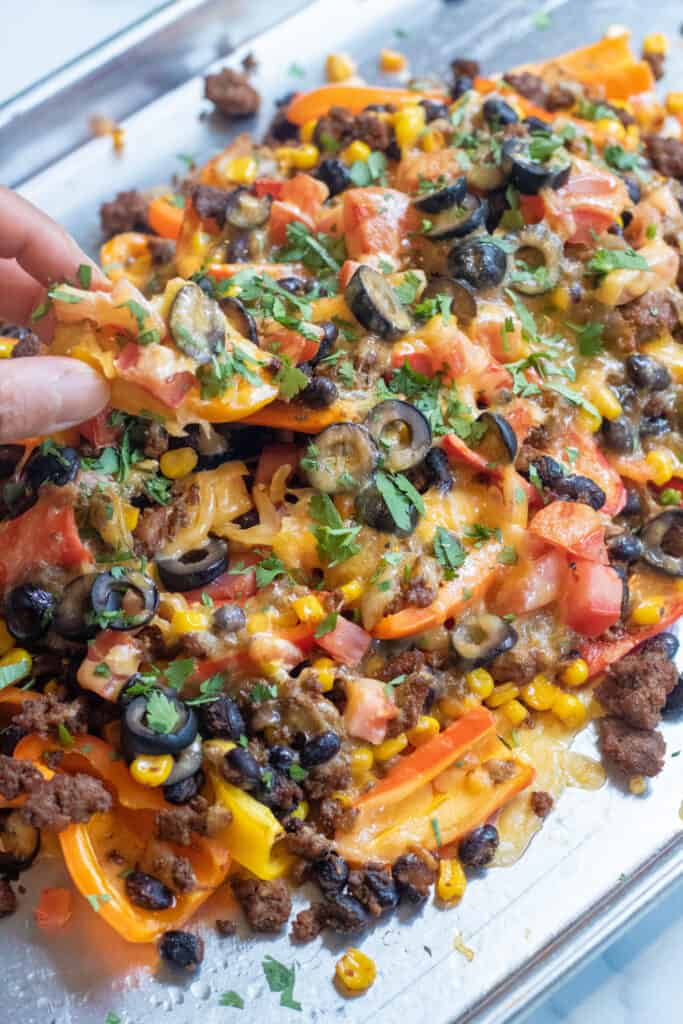 a baking sheet of mini peppers with ground beef, olives, black beans, corn, melted cheese, and fresh cilantro nachos.