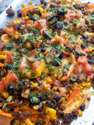 a baking sheet of mini peppers with ground beef, olives, black beans, corn, melted cheese, and fresh cilantro nachos.