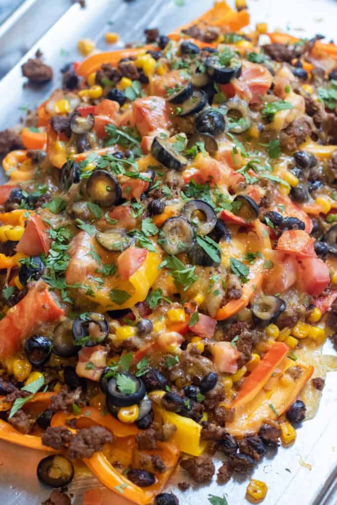 a baking sheet of mini peppers with ground beef, olives, black beans, corn, melted cheese, and fresh cilantro nachos.