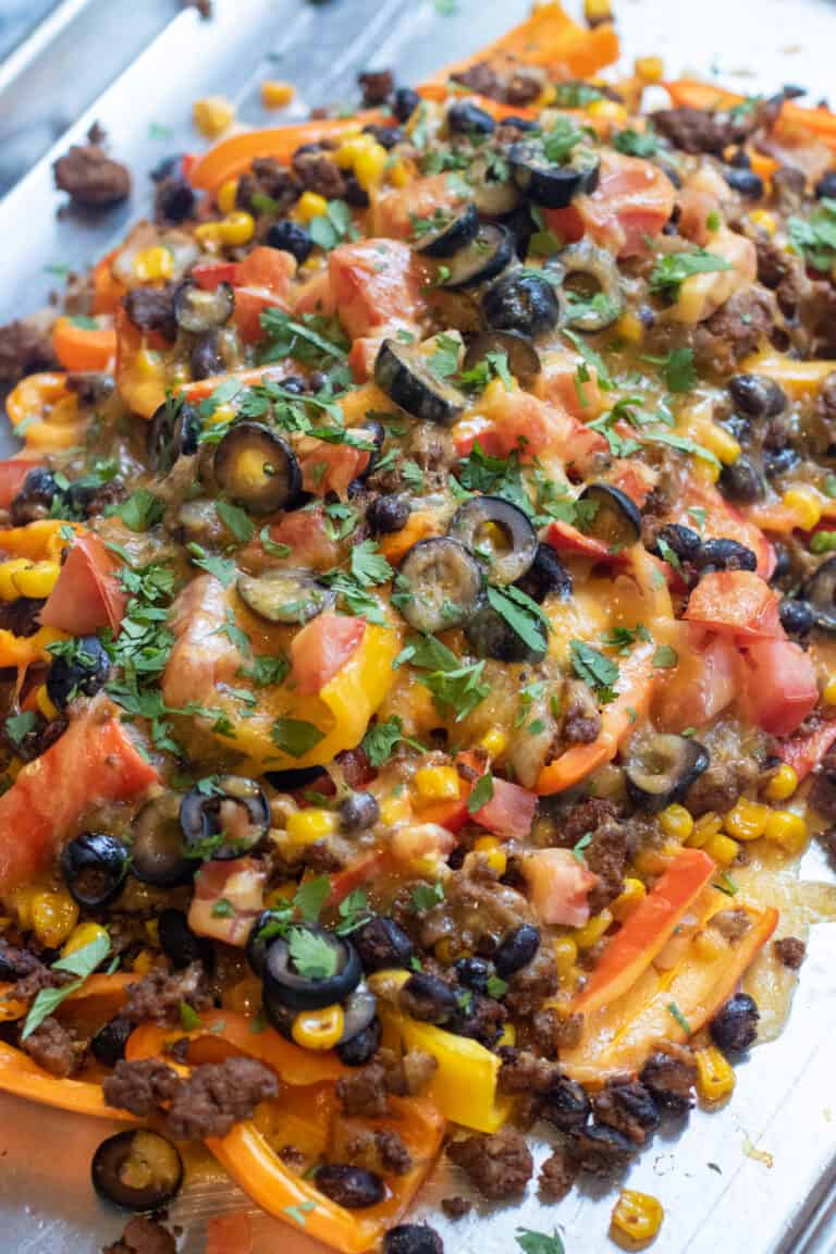a baking sheet of mini peppers with ground beef, olives, black beans, corn, melted cheese, and fresh cilantro nachos.