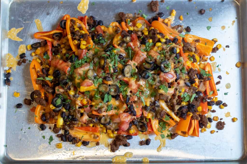 a baking sheet of mini peppers with ground beef, olives, black beans, corn, melted cheese, and fresh cilantro nachos.