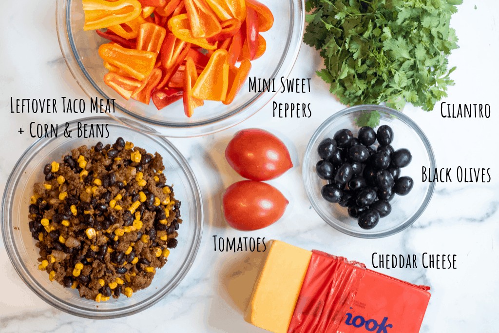 sweet peppers, cilantro, meat mixed with black beans and corn, brick of cheese, tomatoes, and black olives on a counter.