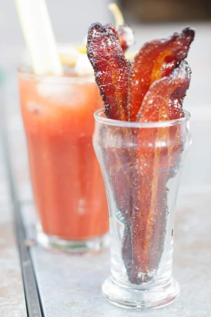 cup of candied bacon in front of a bloody mary