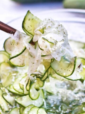 a bowl of thinly sliced cucumbers and onion salad with chopsticks holding it up.