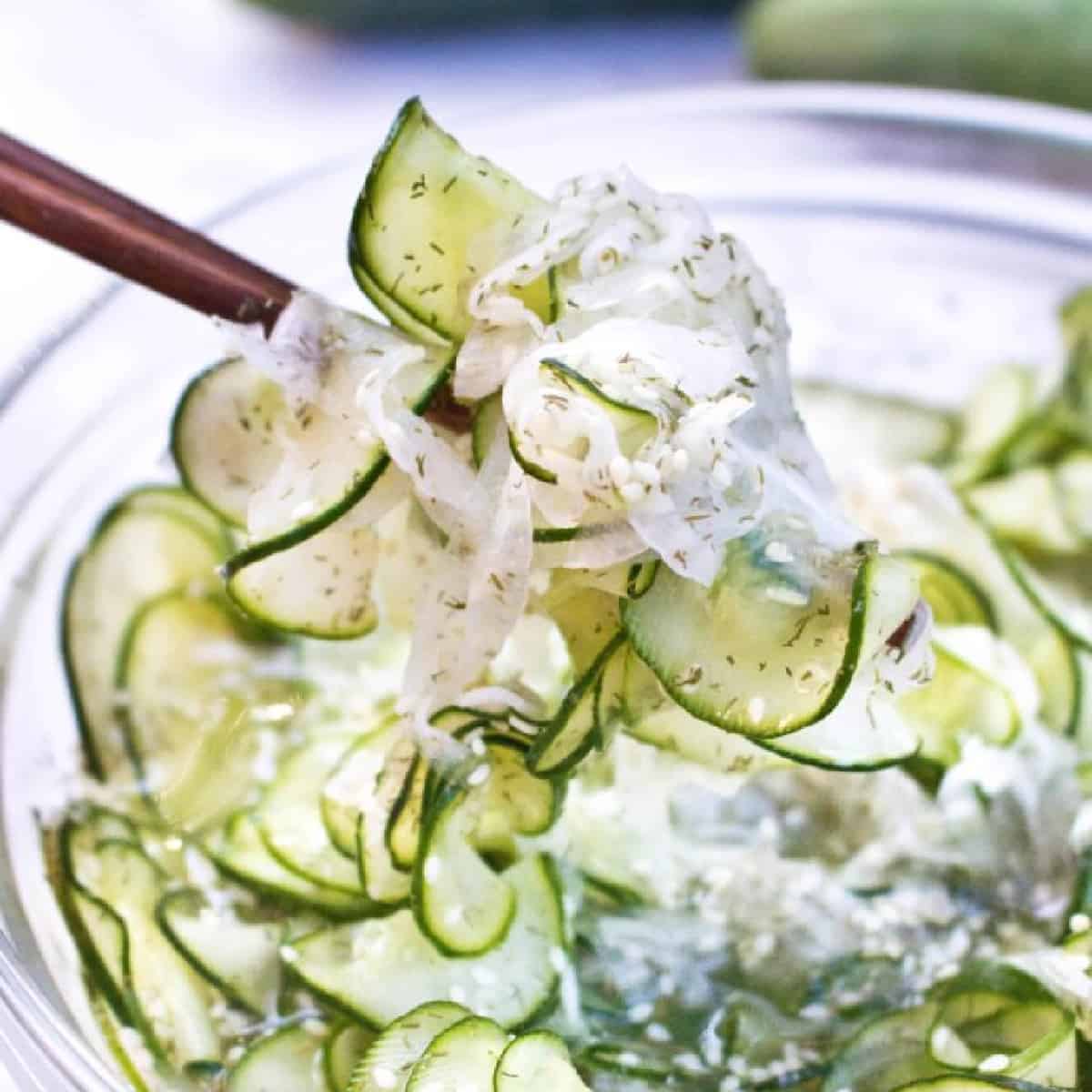 a bowl of thinly sliced cucumbers and onion salad with chopsticks holding it up. 