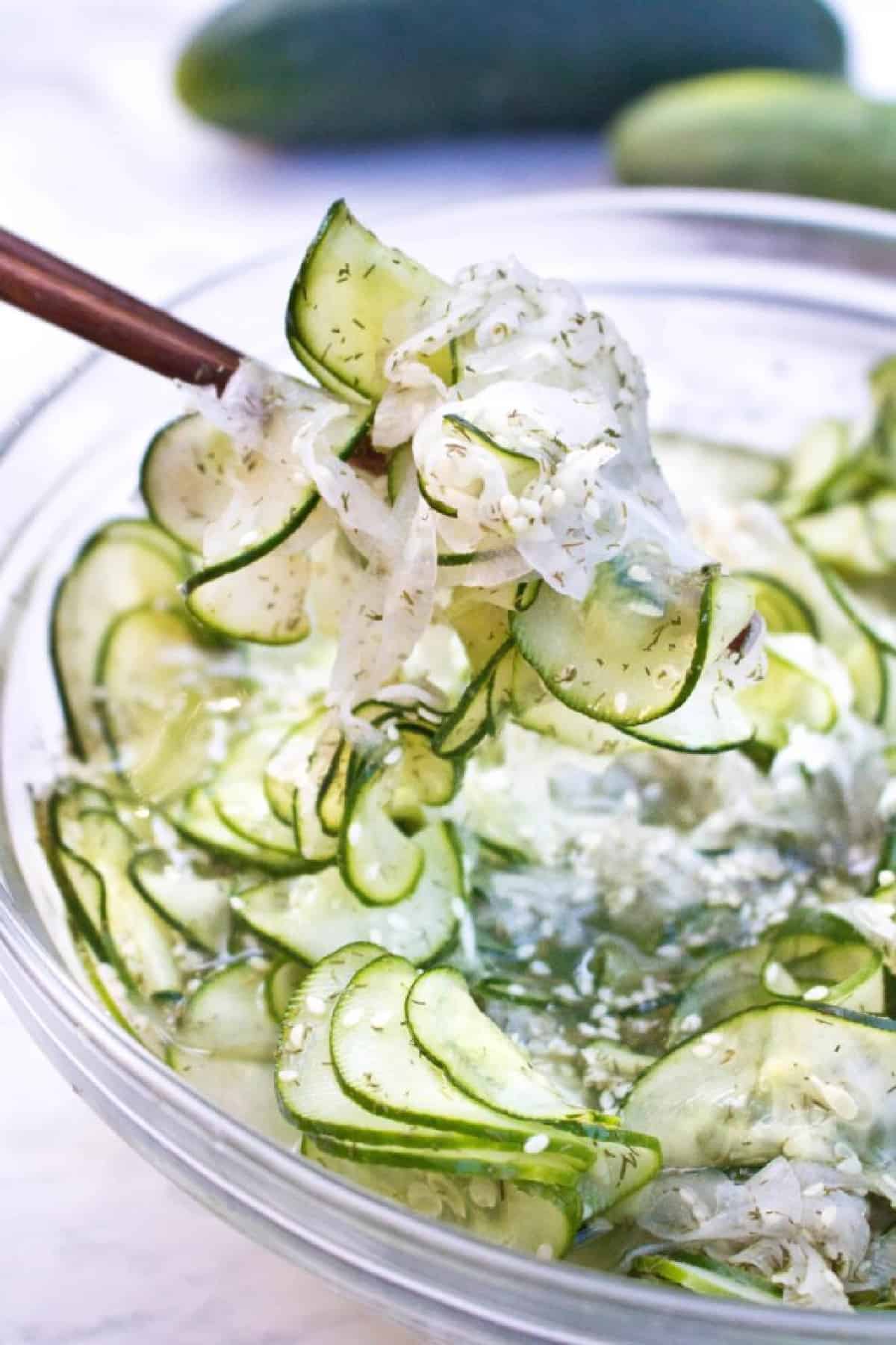 a bowl of thinly sliced cucumbers and onion salad with chopsticks holding it up.