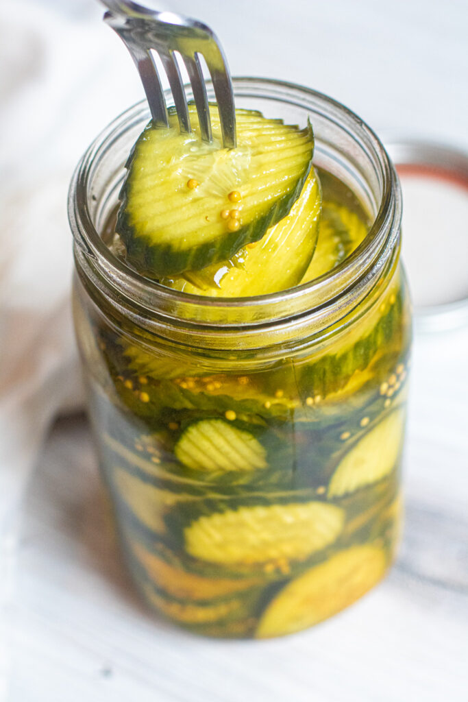 a large jar of pickles with a fork spearing some out.