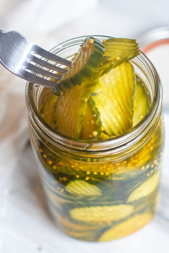 a large jar of pickles with a fork spearing some out.