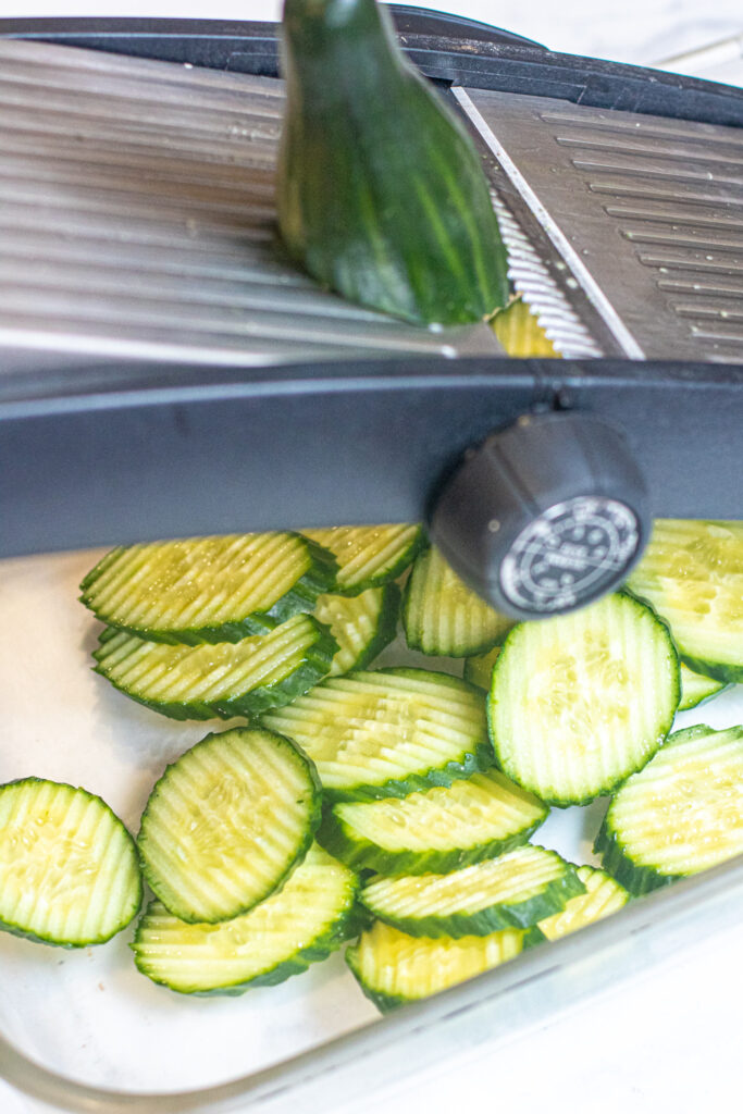 a cucumber being sliced on a mandolin and cucumber slices.