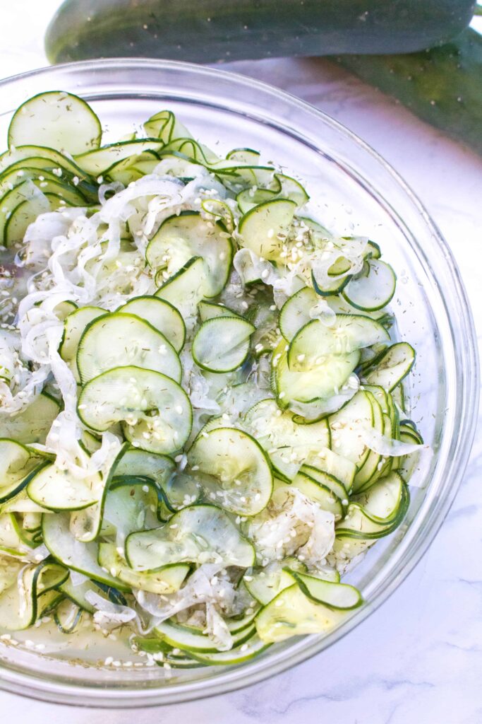 large bowl with sliced cucumbers, onions, and sesame seeds.