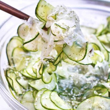 chopsticks holding thinly sliced cucumbers in a bowl.
