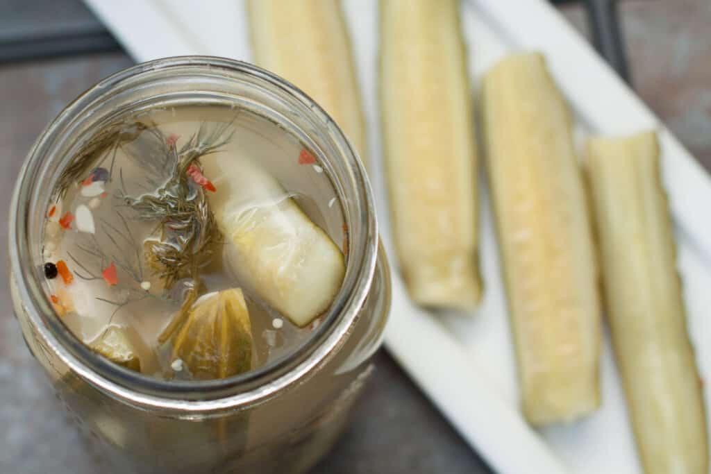 an open jar and dill pickle spears on plate.