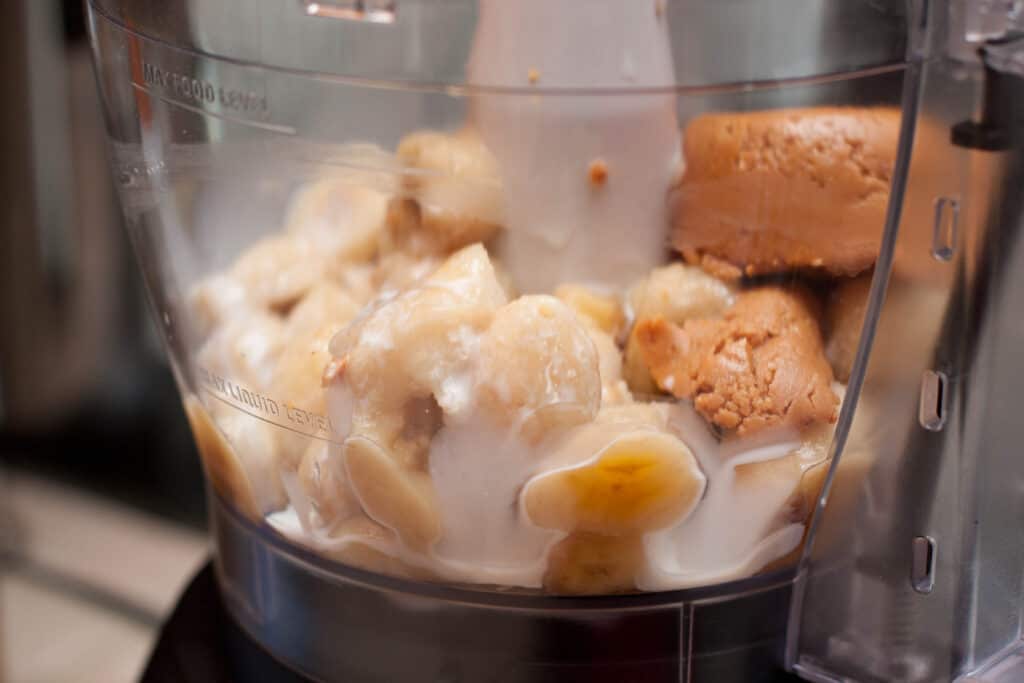a blender with bananas and peanut butter with some cream.