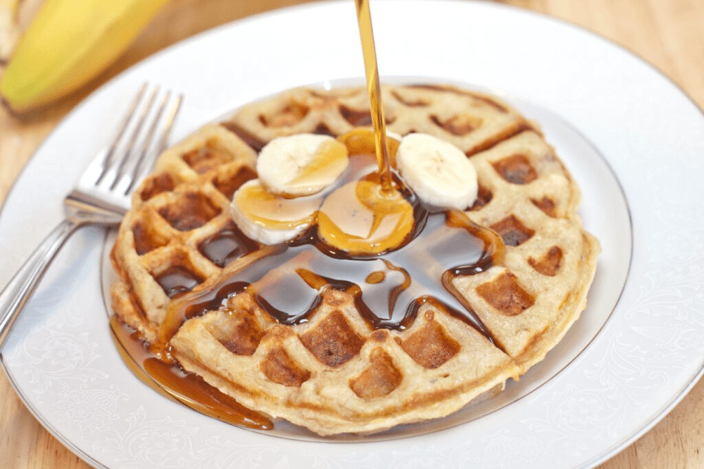 maple syrup being poured on banana waffles.