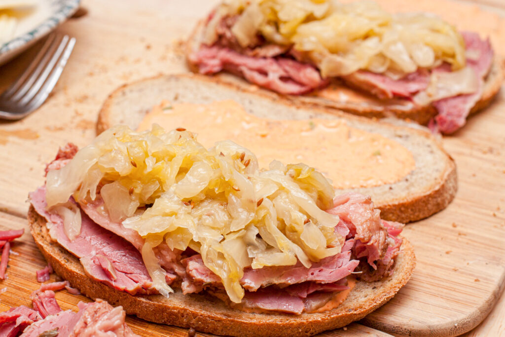 a Reuben sandwich being assembled with rye bread, corned beef, sauerkraut