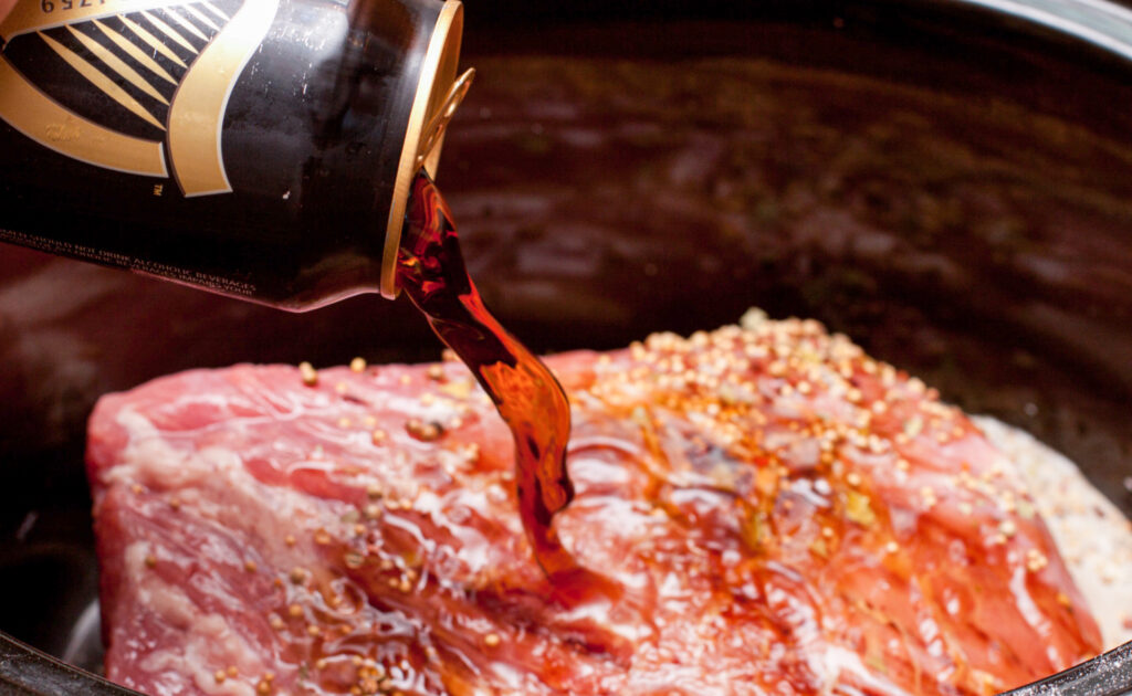 corned beef in a crock pot with stout beer being poured on