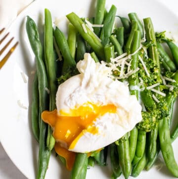 two plates with green beans and pesto and topped with a runny poached egg.