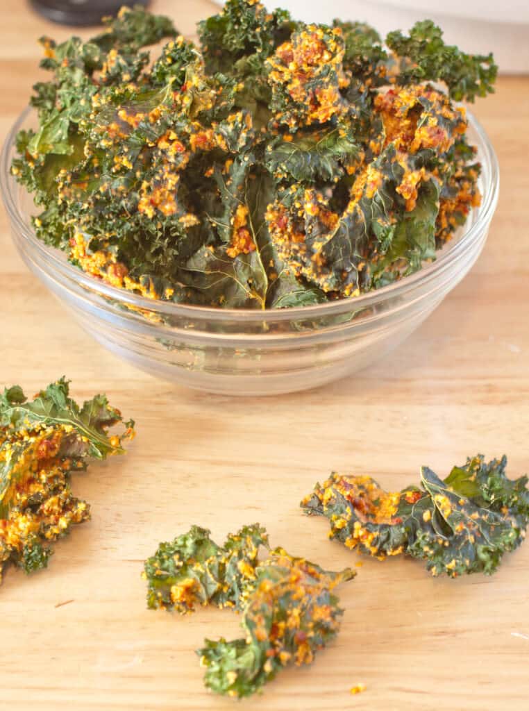 a bowl with coated kale chips and a few on the counter.