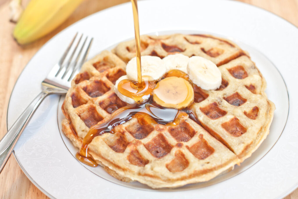 a round waffle on a plate with sliced bananas and syrup being poured on top.