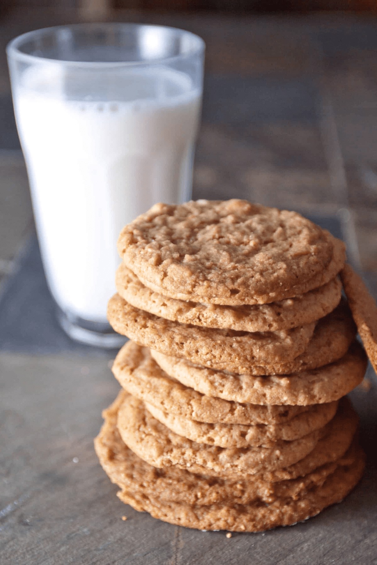 a stack of thin cookies in front of a glass of milk.