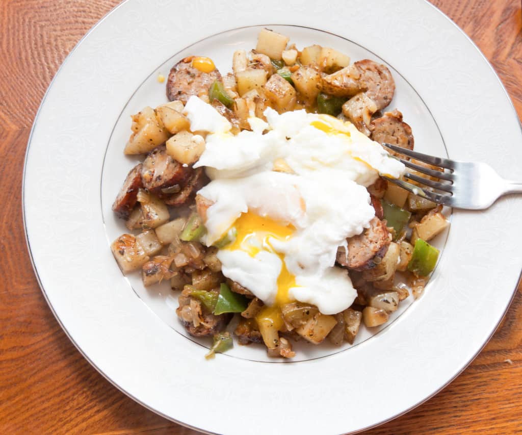 a plate with runny eggs, potaties, peppers, and sausage.