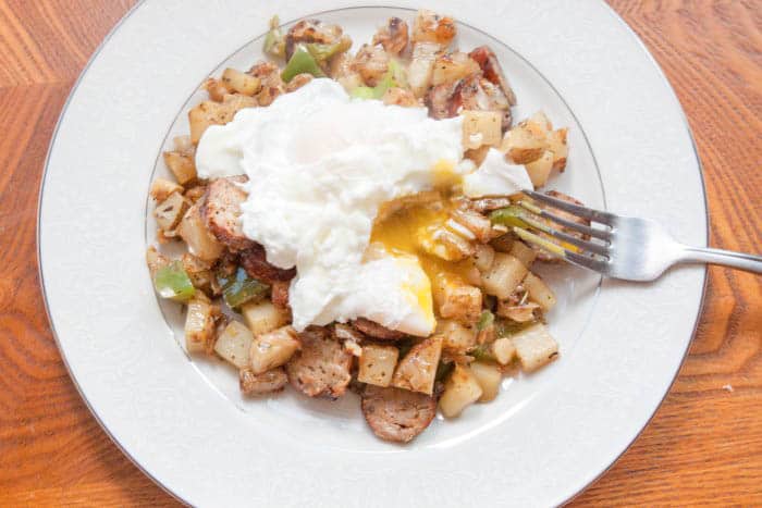 a plate of potatoes and peppers and sausage with a broken yolk egg.