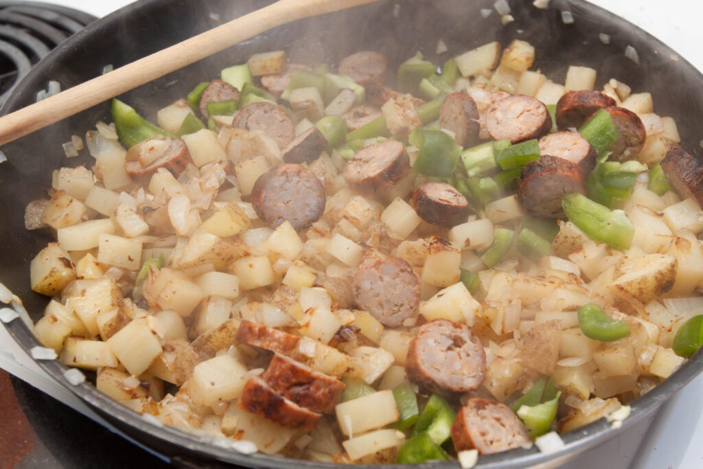 potatoes, green bell peppers, sausage cooking in a pan.