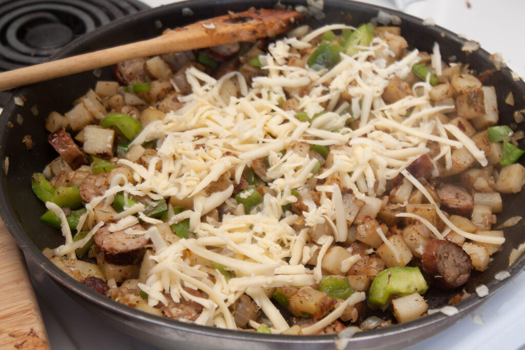 a pan of cooked sausage, eggs, peppers, topped with shredded cheese.