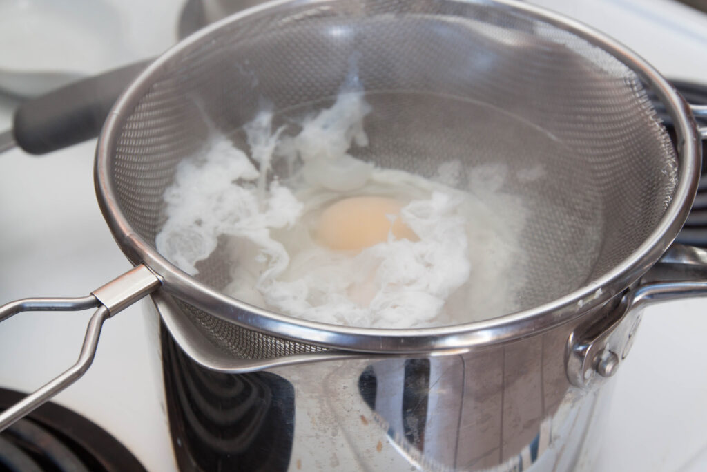 a sieve in a pot with poaching eggs.