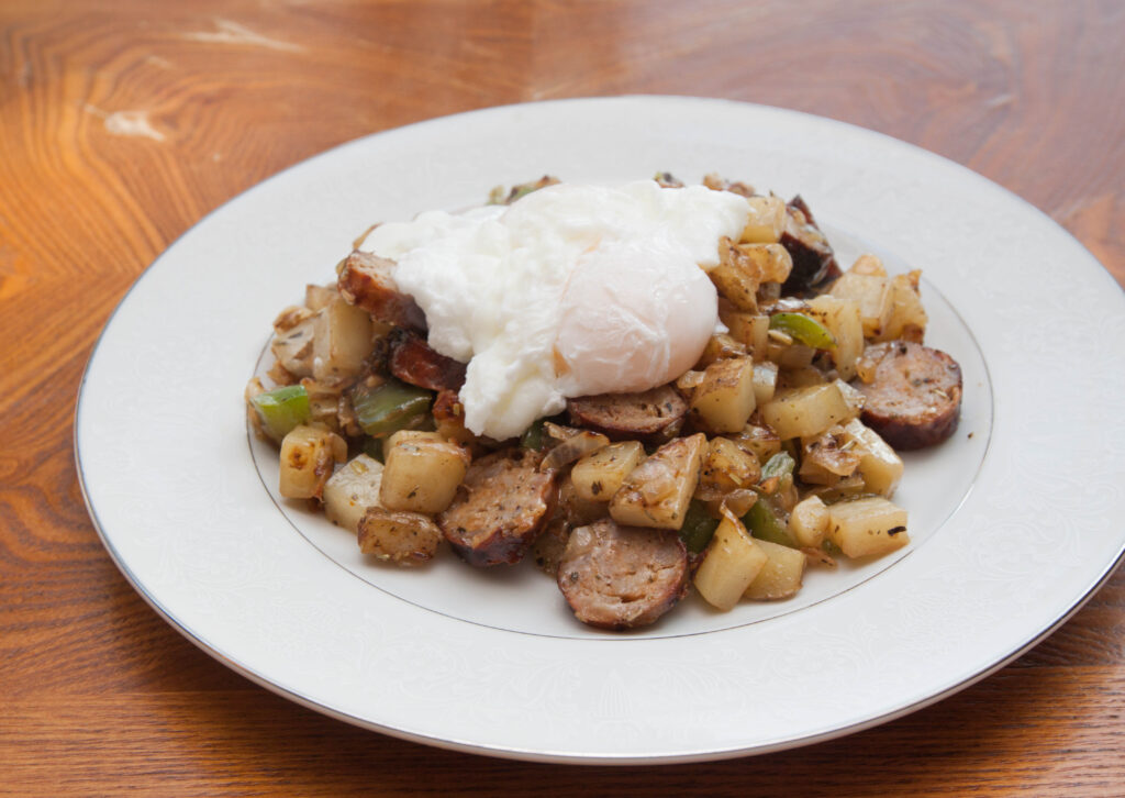 a plate of potatoes, sausage, topped with poached egg.