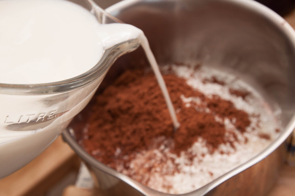 milk being poured into a pan with cocoa powder.