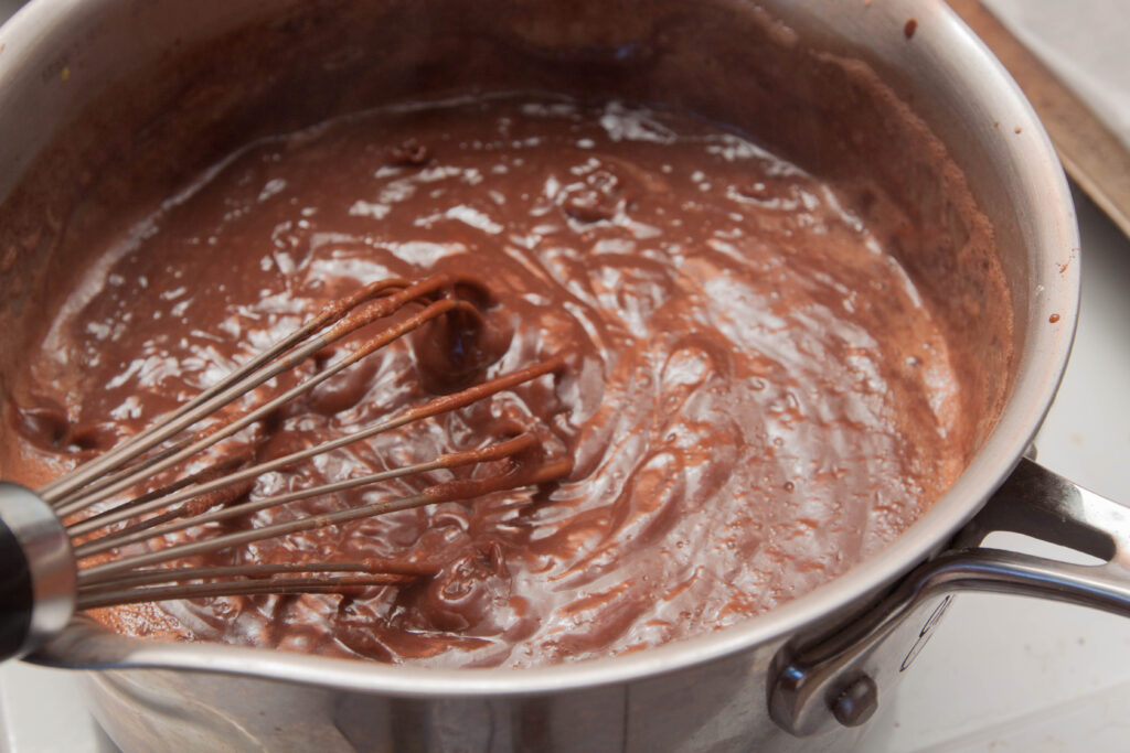 a whisk in a pot of thickened chocolate.