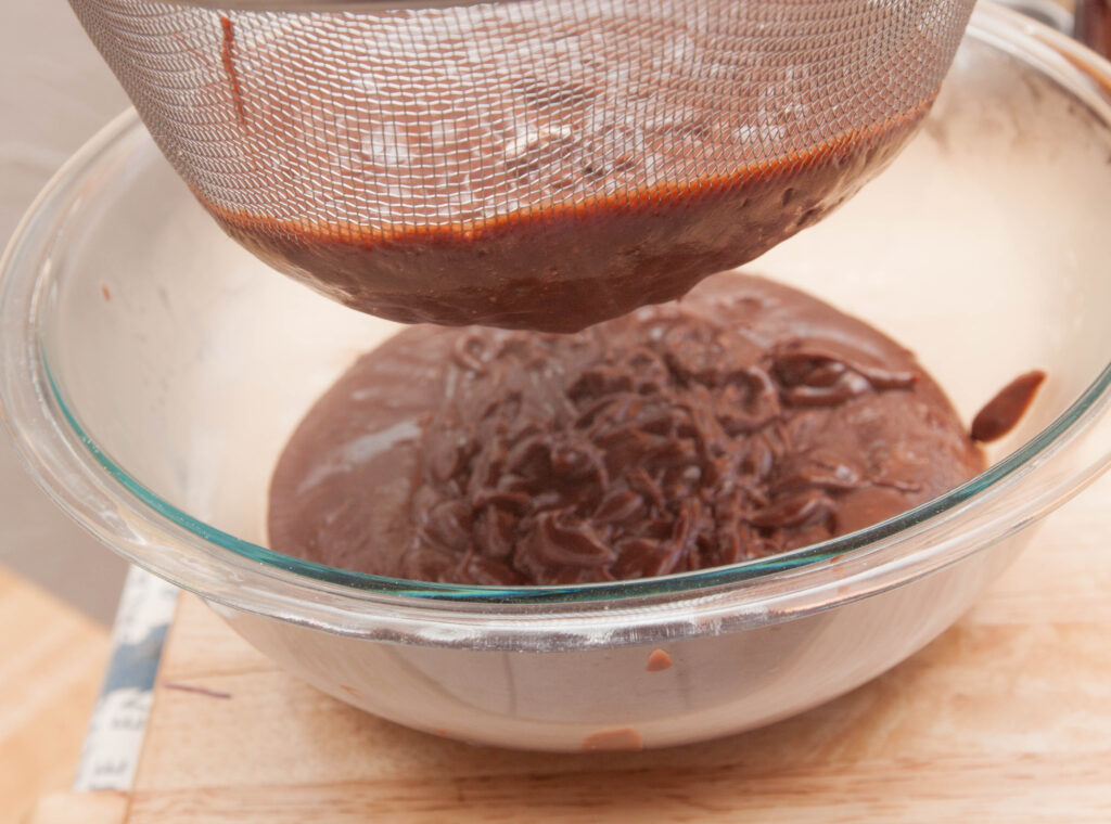 a sieve with chocolate pudding over a large bowl.