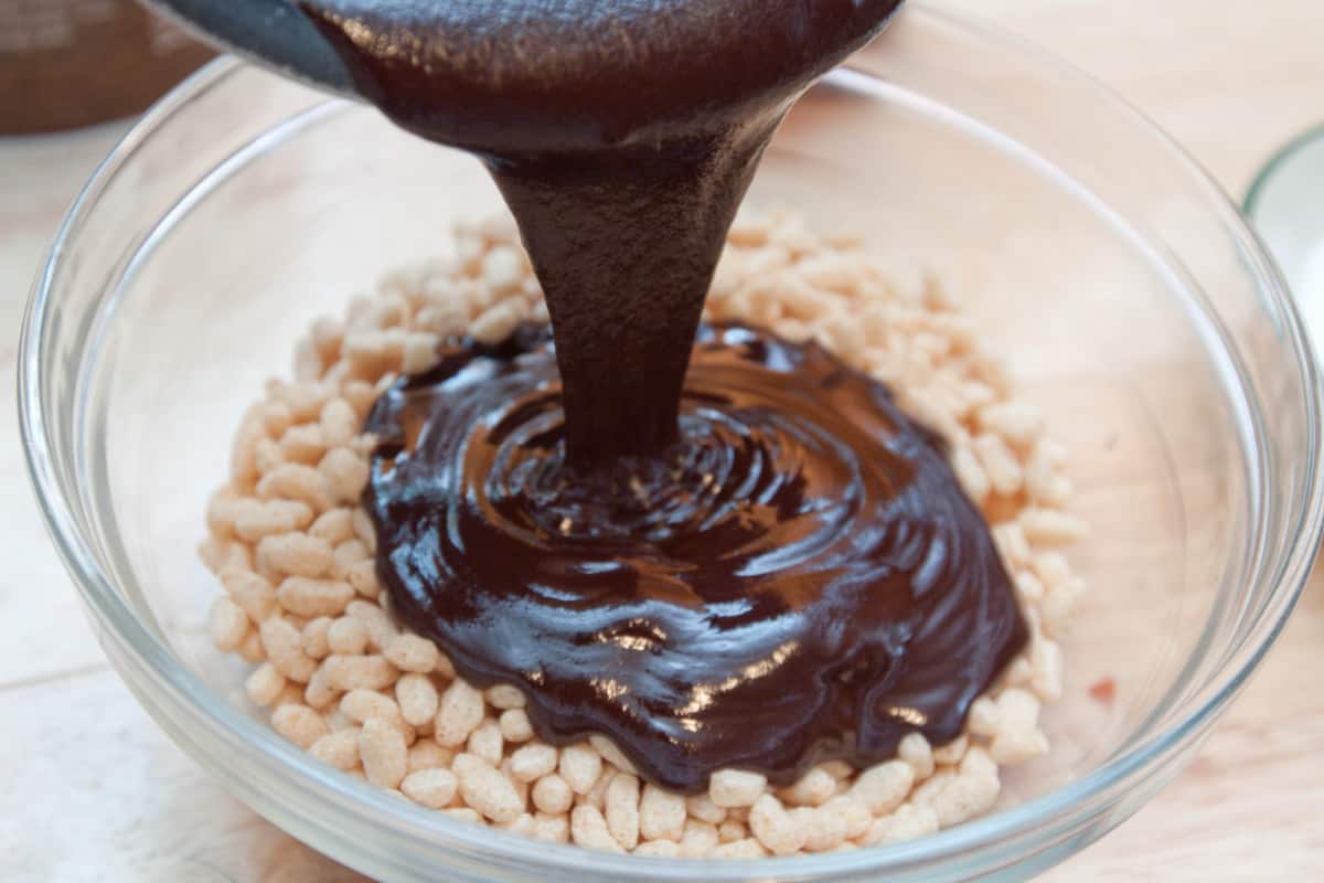 chocolate being poured into a bowl of rice cereal.