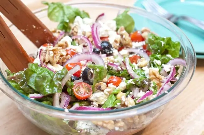 a bowl of salad with tongs.