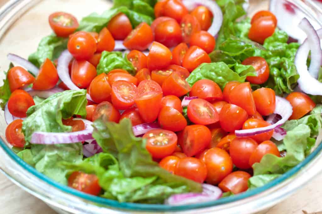 a bowl of salad greens topped with tomatoes.